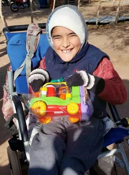 Niño sonriente en silla de ruedas con un trencito de juguete en las manos